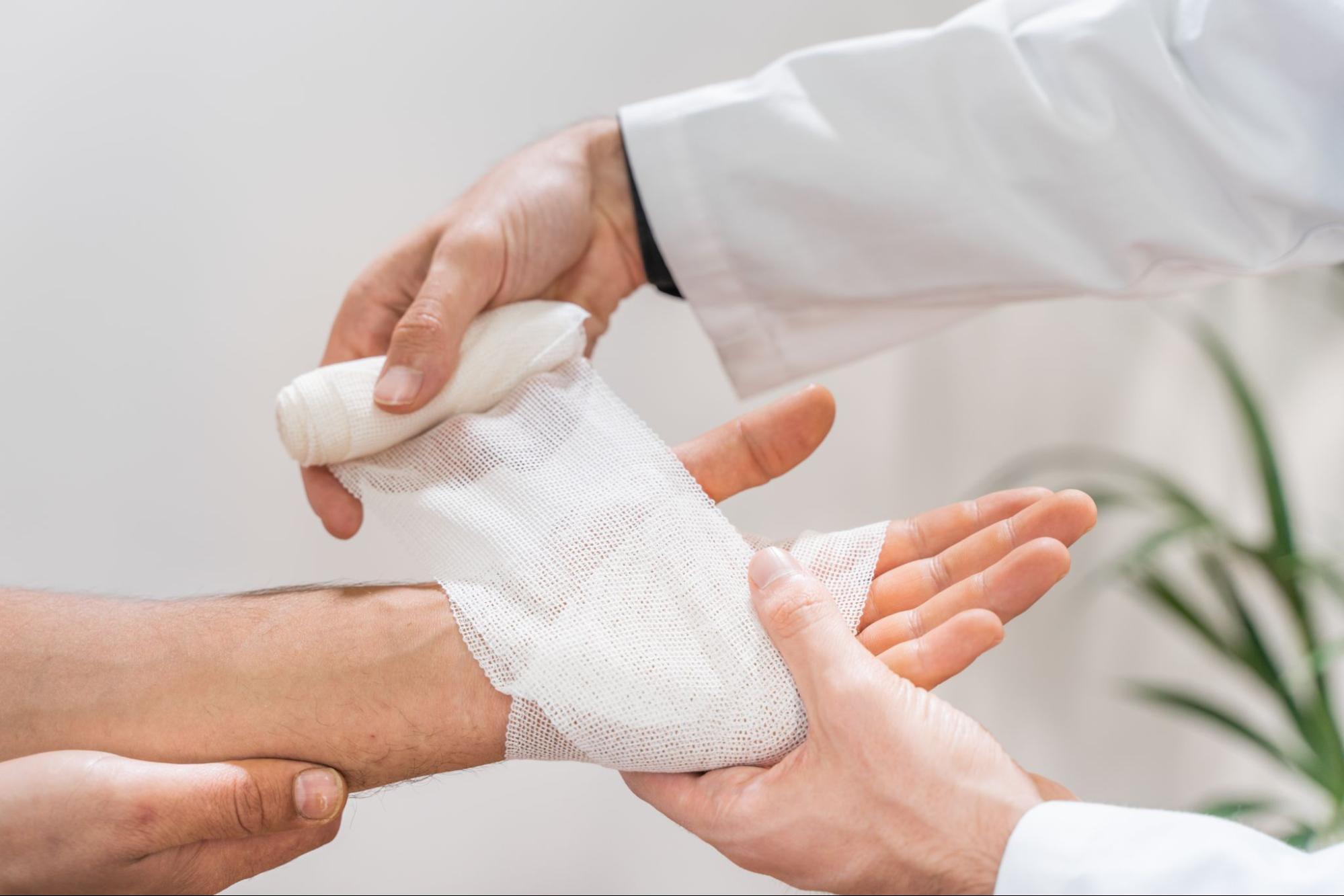 A doctor wrapping a medical bandage around a wound on a man’s hand.