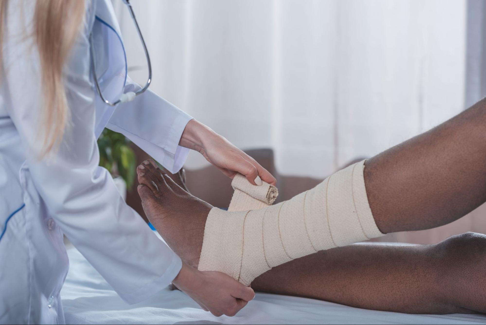 A female doctor in a hospital treating pressure ulcer symptoms by bandaging a man’s heel and ankle.