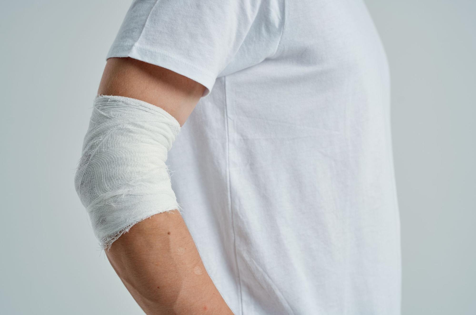 A patient in a white t-shirt with a white bandage over his elbow.
