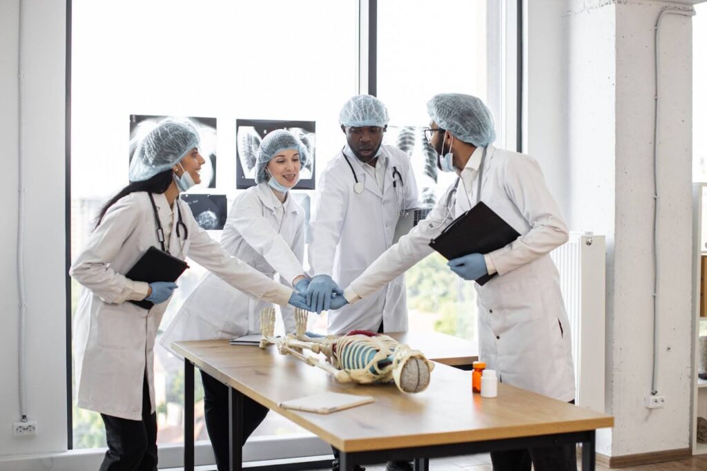 Doctors unite hands over an artificial skeleton and X-ray images during a regenerative medicine consultation.