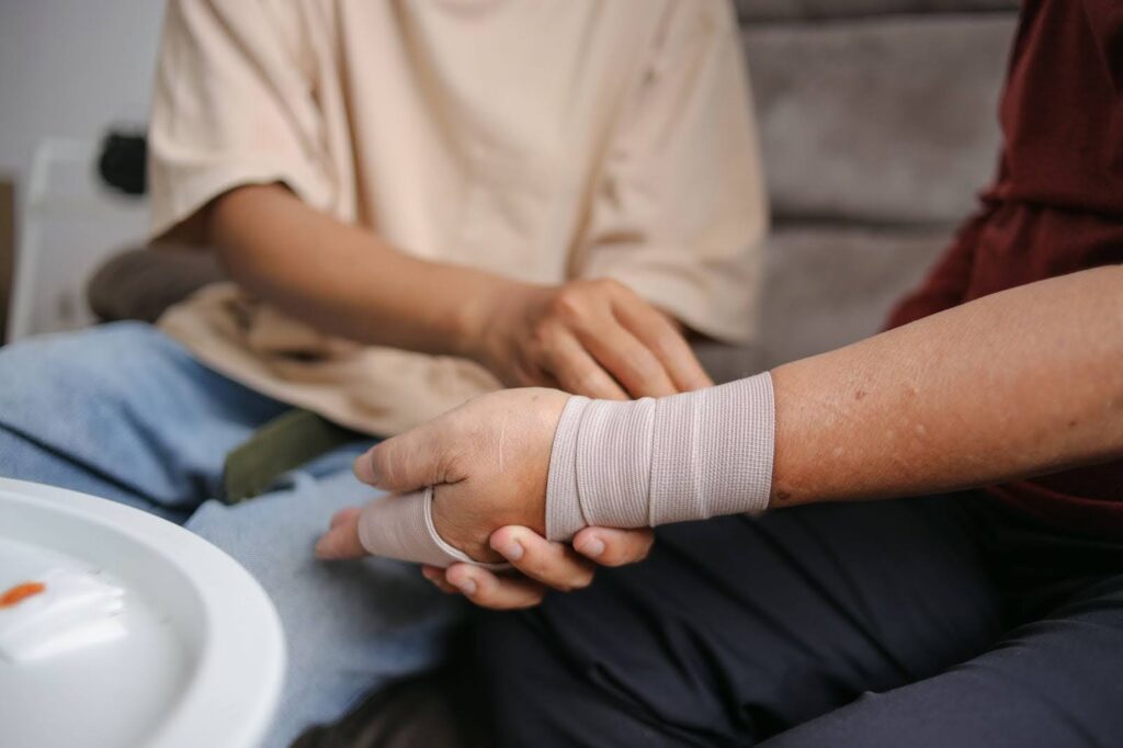 A man is helping another man wrap a bandage around the wounds on his wrist.
