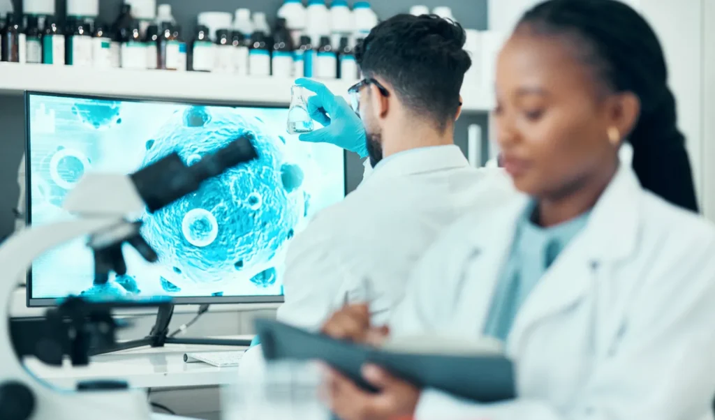 Two scientists look at models of cells and examine slides under a microscope.