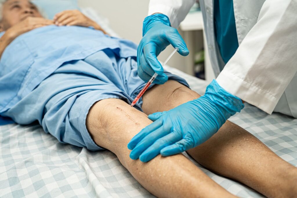 Doctor injecting hyaluronic acid and PRP into a senior woman’s knee after surgery to aid healing and prevent infection.